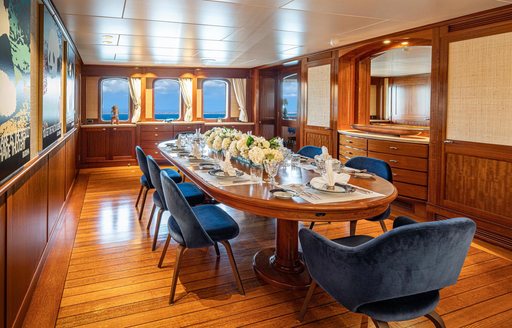 Interior dining area with long table and blue upholstered chairs onboard charter yacht ASTERIA