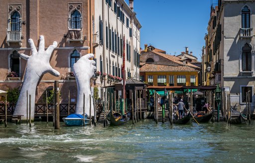 Hands climbing out of the water onto a building as part of an art exhibit in Venice