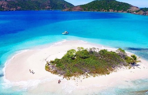 A small white sand island surrounded by cobalt blue waters in the BVIs