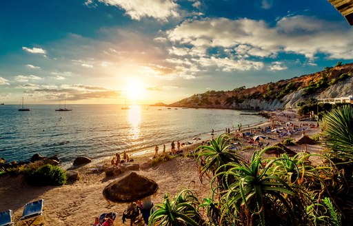 People sunbathing on sandy beach in Ibiza as sun sets