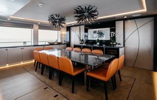 Interior dining table surrounded by orange seats adjacent to large windows