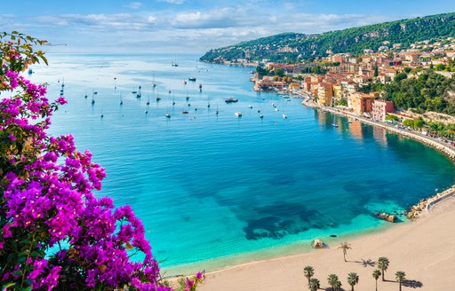 french curved sand beach against a blue sea dotted with yachts