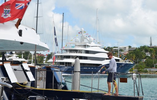 crew member walks onto yacht with superyacht AMARYLLIS in the background in Antigua