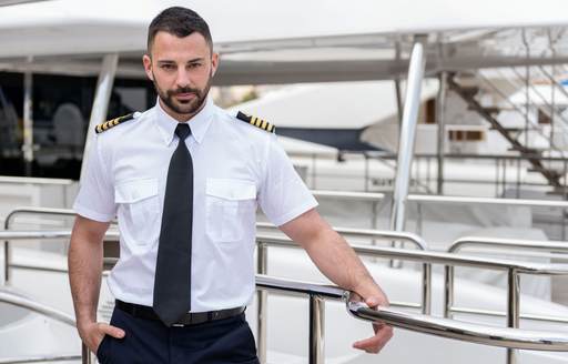 A captain poses next to a yacht