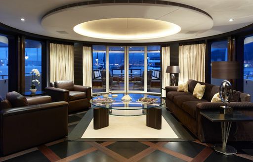 deep brown armchairs and sofas flanked by full-length windows in the skylounge aboard luxury yacht ROCKET 