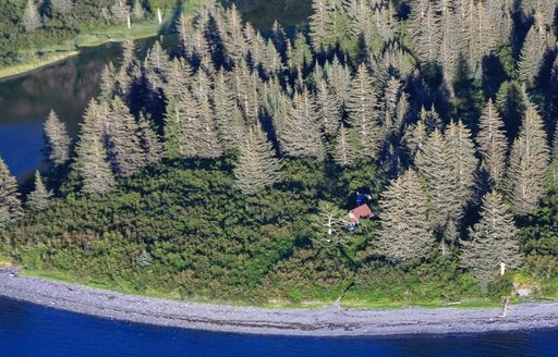 An aerial view of a cabin in a green forest next to blue coast