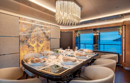 Interior dining area with a long table and upholstered cream seats, prepped for a meal onboard charter yacht SUNRISE