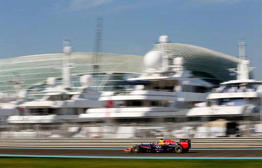 Car on Yas Marina racetrack goes past superyachts lined up at berth during Abu Dhabi Grand Prix