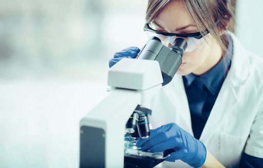 A lab assistant looks into a microscope