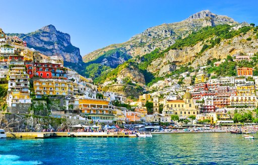 the candy colour houses on the hill of the amalfi coast rolling down to the seafront where there are many berthing spots for superyachts that are on their luxury yacht charter vacation through the Mediterranean 