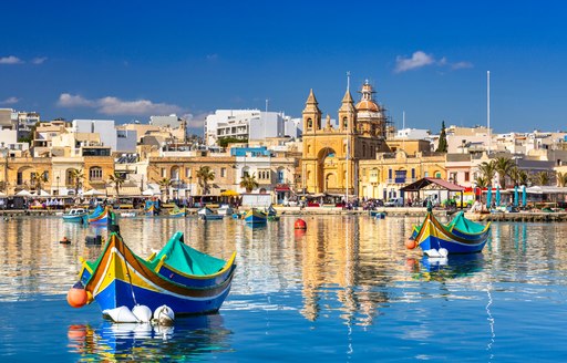 Small fishing boats moored in a clam harbor in Malta with historical buildings in the background