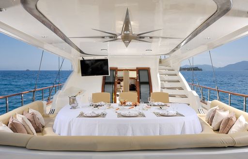 Alfresco dining setup onboard Sailing yacht charter ALESSANDRO I, dining table with white tablecloth adjacent to U-shaped seating 