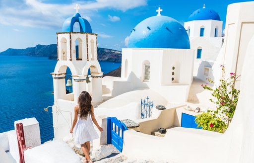 blue and white village in santorini, woman walks along steps overlooking the ocean
