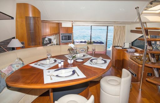 Interior dining area onboard private yacht charter MEDITERRANI IV, oval dining table surrounded by a cream bench and standalone seats