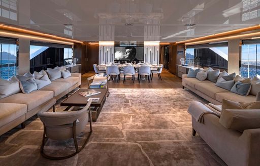 Interiors onboard charter yacht ENTERPRISE, spacious main salon with sofas along either side and a dining table aft