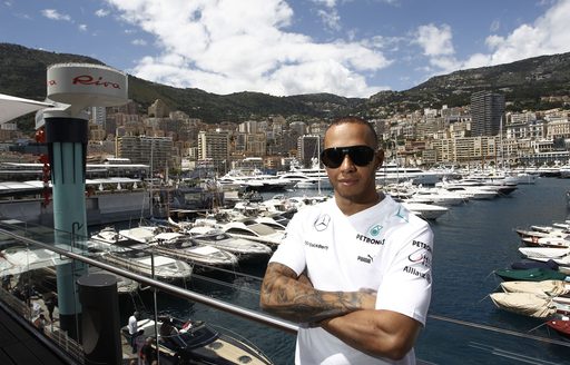 Lewis Hamilton standing in front of Port Hercule with many chartert yachts berthed 