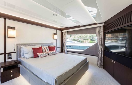Overview of the master cabin onboard charter yacht NEW EDGE, central berth facing flatscreen TV with large window in the background 