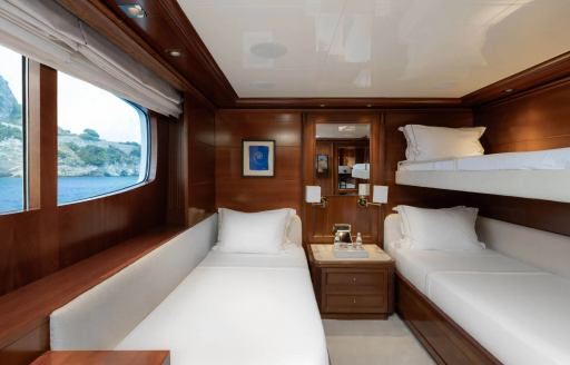 Guest cabin onboard luxury charter yacht EMIR, with a single bed underneath a window and bunks adjacent