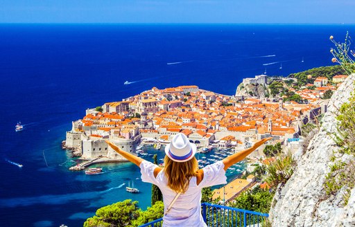 A woman stands with arms outstretched on a hilltop village overlooking Dubrovnik, Croatia