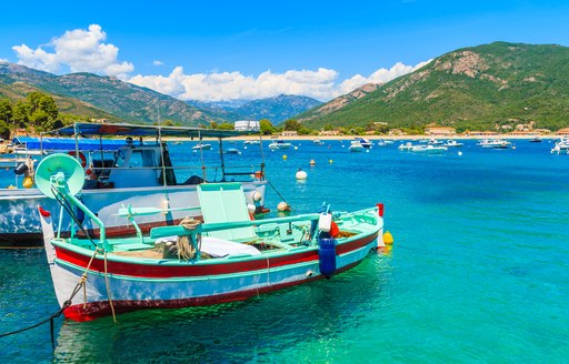 Small, colorful wooden fishing boats tied up in an idyllic blue-green harbor in Corsica