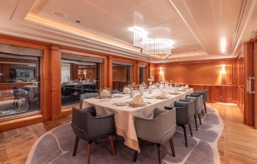 Dining room onboard charter yacht CARINTHIA VII, long table surrounded by gray upholstered tub chairs