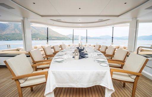 Alfresco dining set up onboard charter yacht FORTUNA, central long table with white tablecloth, surrounded by white upholstered chairs