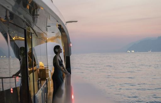 Woman stands on deck of charter yacht VIVALDI looking out over the sea as the sun sets