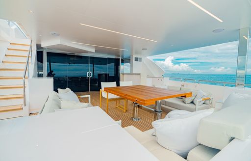 Aft deck onboard luxury yacht rental SEA-RENITY, with plush white seating and an alfresco dining set up