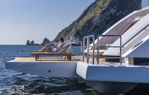 Woman reclines on swim platform of luxury yacht DRAGON
