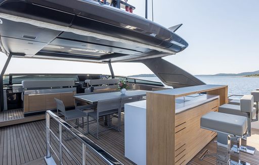 Overview of the flybridge onboard charter yacht JICJ, alfresco dining option with a wet bar in the foreground and some gray stools.