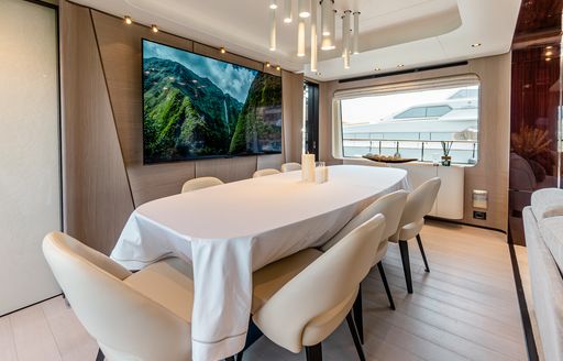 Interior dining area onboard charter yacht VESTA, long table with white tablecloth and adjacent large window