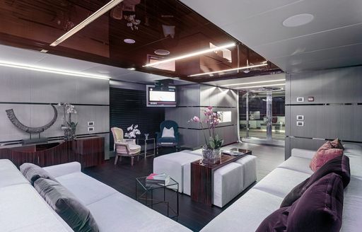 main salon of luxury charter yacht giraud, with cream corner sofas and glossy mahogany ceiling 