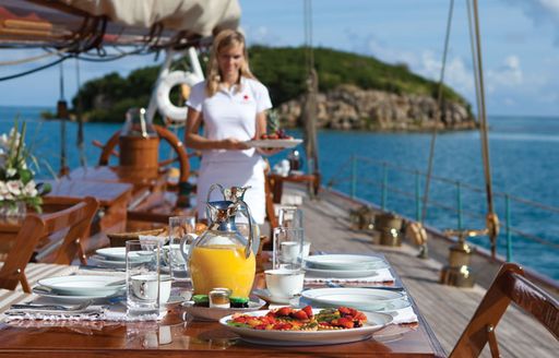 table set for dinner with crew member bringing dishes out on the deck of luxury yacht ELENA