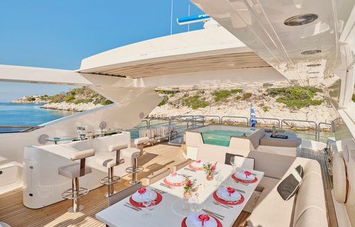 Alfresco dining set up on the flybridge of charter yacht MAKANI II, dining table in the foreground with a wet bar to port side