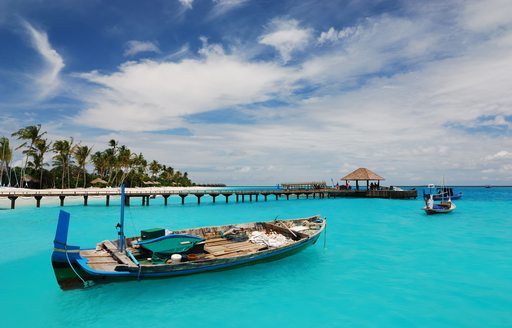 A traditional wooden boat bobs on turquoise waters near a resort pontoon in the Maldives