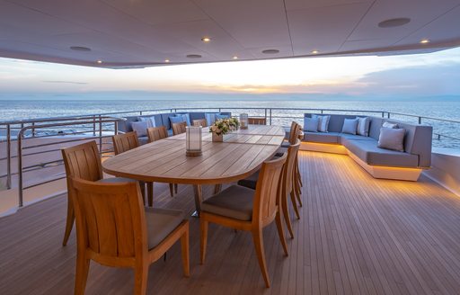 Alfresco dining setup onboard charter yacht AQUA LIBRA, with long dining table center and sweeping view of the sea at sunset