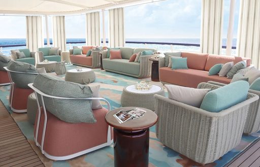Overview of the lounge area in the main salon onboard charter yacht TATOOSH, pastel seating facing in to three round coffee tables 