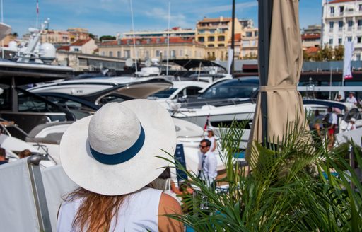 Female visitor to the Cannes Yachting Festival wearing a white, brimmed hat while looking out over the marina.