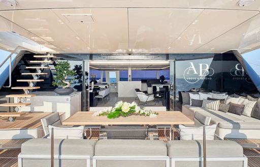 Overview of the aft main deck onboard charter yacht ABOVE & BEYOND, alfresco lounge and dining area with staircase to port leading up to upper deck
