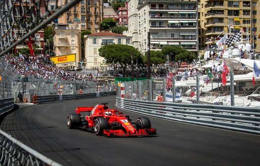 Car on the track at the Monaco Grand Prix with superyachts in background