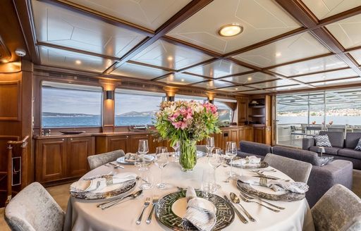 Interior dining area onboard charter yacht KLOBUK, circular table laid for a meal with floral centerpiece