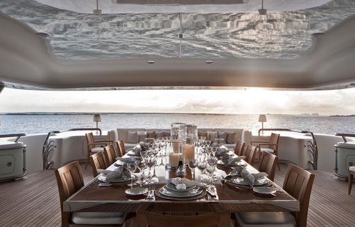 Fully laid out dining table on deck of charter yacht Lady E with sunning setting on horizon
