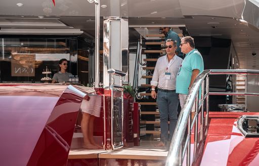Visitors at the Monaco Yacht Show talking on the aft deck of a berthed superyacht