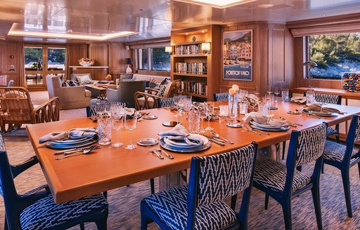 Dining area in the main salon onboard charter yacht NATALIA V, with lounge and bookshelves in the background