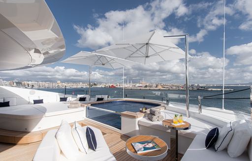 Overview of an aft deck onboard charter yacht RESILIENCE with a glass sided Jacuzzi surrounded by plush white seating and a sunpad