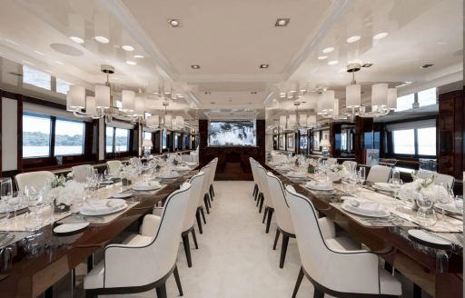 Large dining room onboard luxury charter yacht EMIR, twin long tables surrounded by white upholstered chairs and many windows