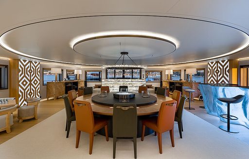 Formal dining area onboard charter yacht LA DATCHA with a round table surrounded by autumnal upholstered chairs