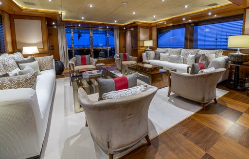 Interiors onboard charter yacht BEHIKE, spacious lounge area with sofas and armchairs facing in, surrounded by wide windows