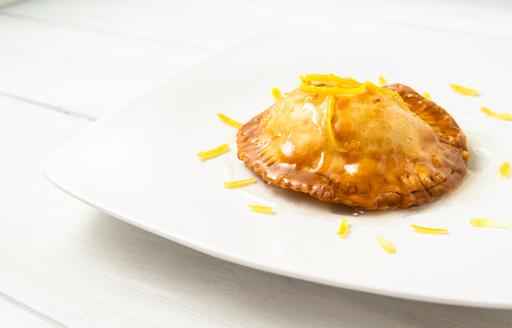 A square white plate with a Sardinian seadas pastry topped with honey