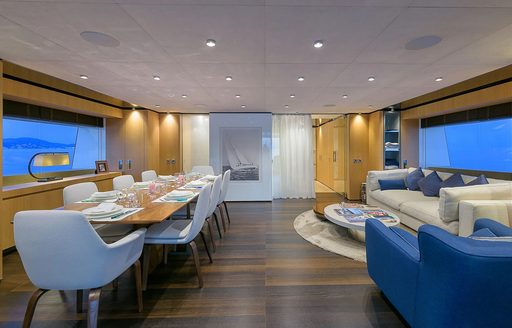 Interior dining area onboard charter yacht MR T, long dining table to port and seating area starboard